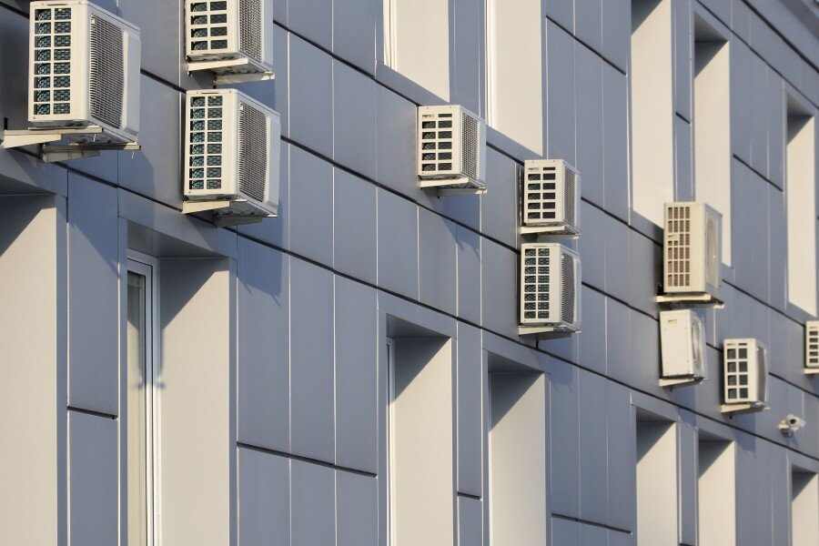 Multiple outdoor air conditioning units mounted on the exterior of a modern commercial building.