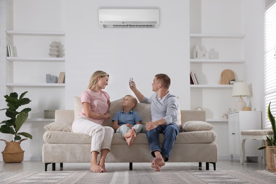 Family on sofa; man activates wall AC with remote for comfortable Australian home.