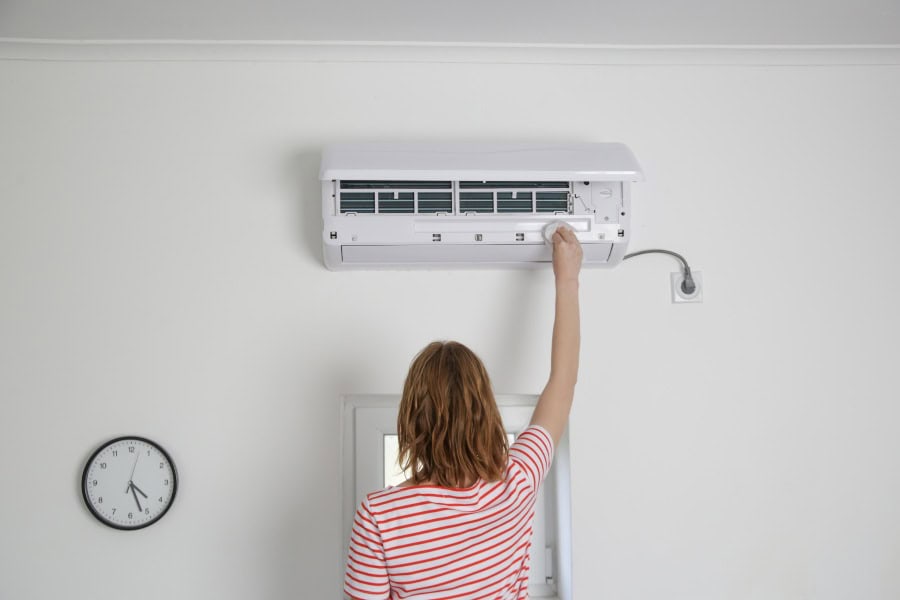 Woman unplugging white wall AC unit from outlet, a key maintenance factor for extending unit lifespan.
