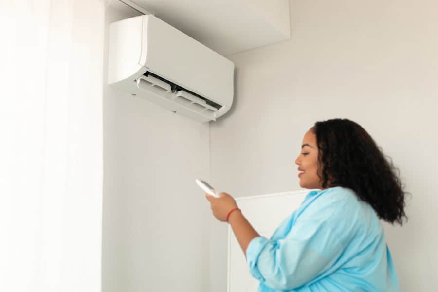 Woman adjusting a split system air conditioner with a remote in a bright room.