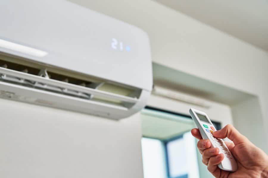 A hand using a remote to adjust a wall-mounted air conditioner indoors.