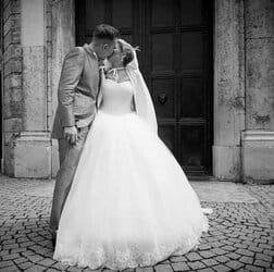 Trauende braut und bräutigam küssen sich vor altem steinmauer-portal hochzeitsfotografie in schwarz-weiß.
