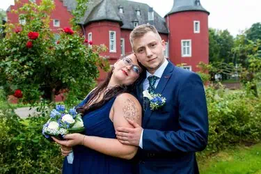 Romantisches Hochzeitsfoto mit Braut und Bräutigam vor einem rot-weißen Schloss in Aachen.
