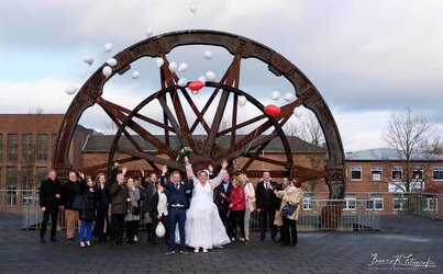 Fröhliche Hochzeitsgesellschaft vor einem historischen Rad in Aachen, feierlich und voller Freude.