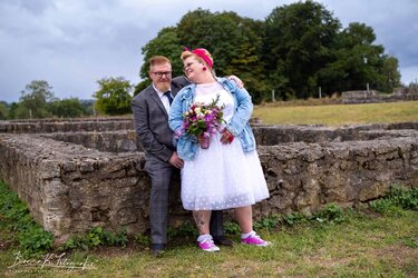 Hochzeitspaar mit Vintage-Charme vor einer alten Steinmauer im Grünen.
