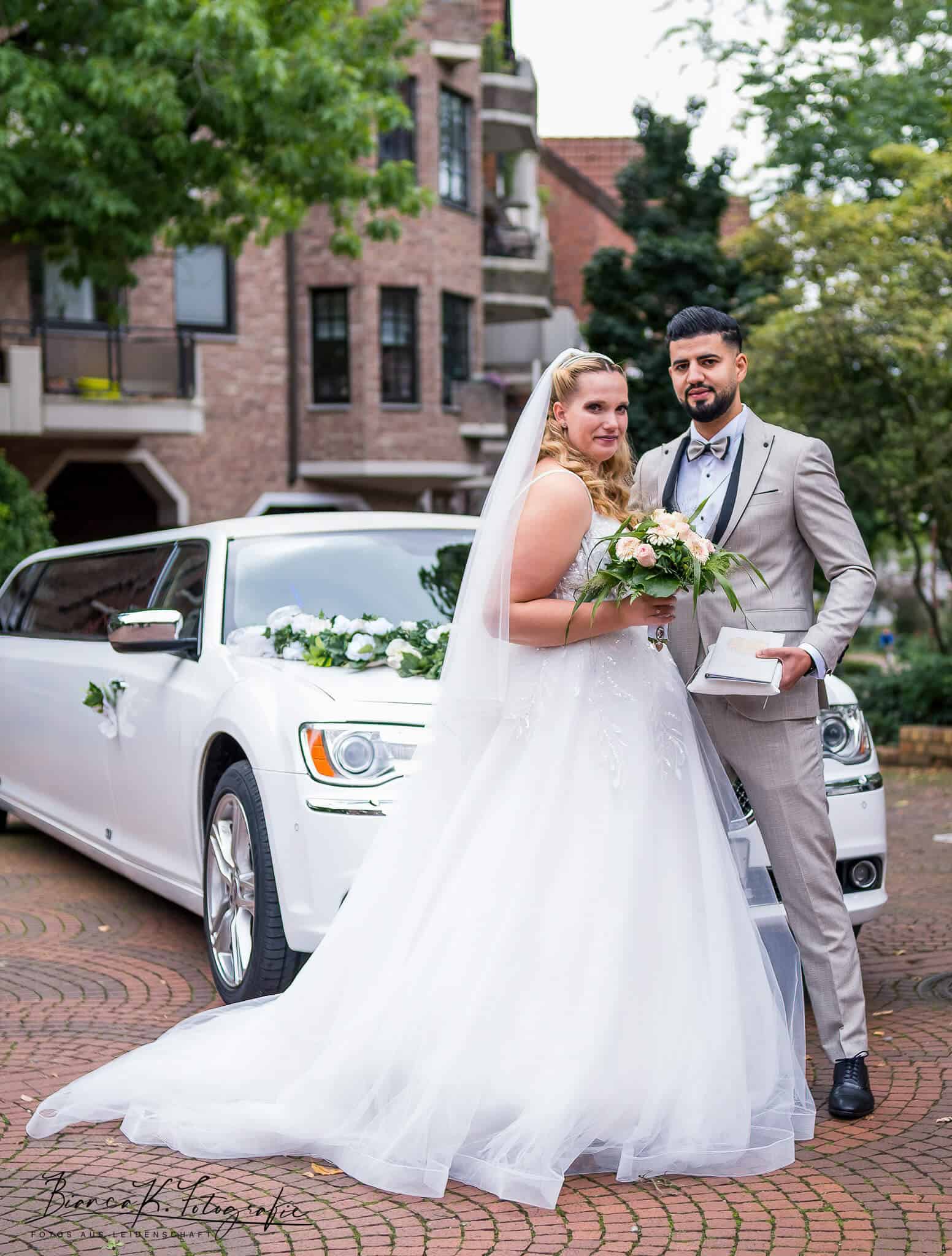 Hochzeitsfotografie mit Braut und Bräutigam vor weißem Auto in Aachen, romantisches Brautpaarshooting im urbanen Umfeld.