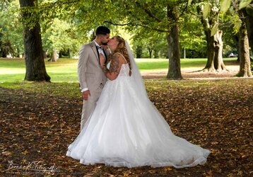 Hochzeitspaar in einem Park, romantischer Kuss, Braut in Trauung, natürliche Kulisse, Liebe.