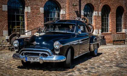 Altes schwarzes Auto vor Ziegelsteinmauer in Aachen, vintage Fahrzeug, historische Autokunst.