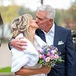 Romantisches Hochzeitsfoto mit Kuss im Freien, Braut mit Blumenstrauß und Bräutigam in Anzug, im Herbst bei Sonnenuntergang.