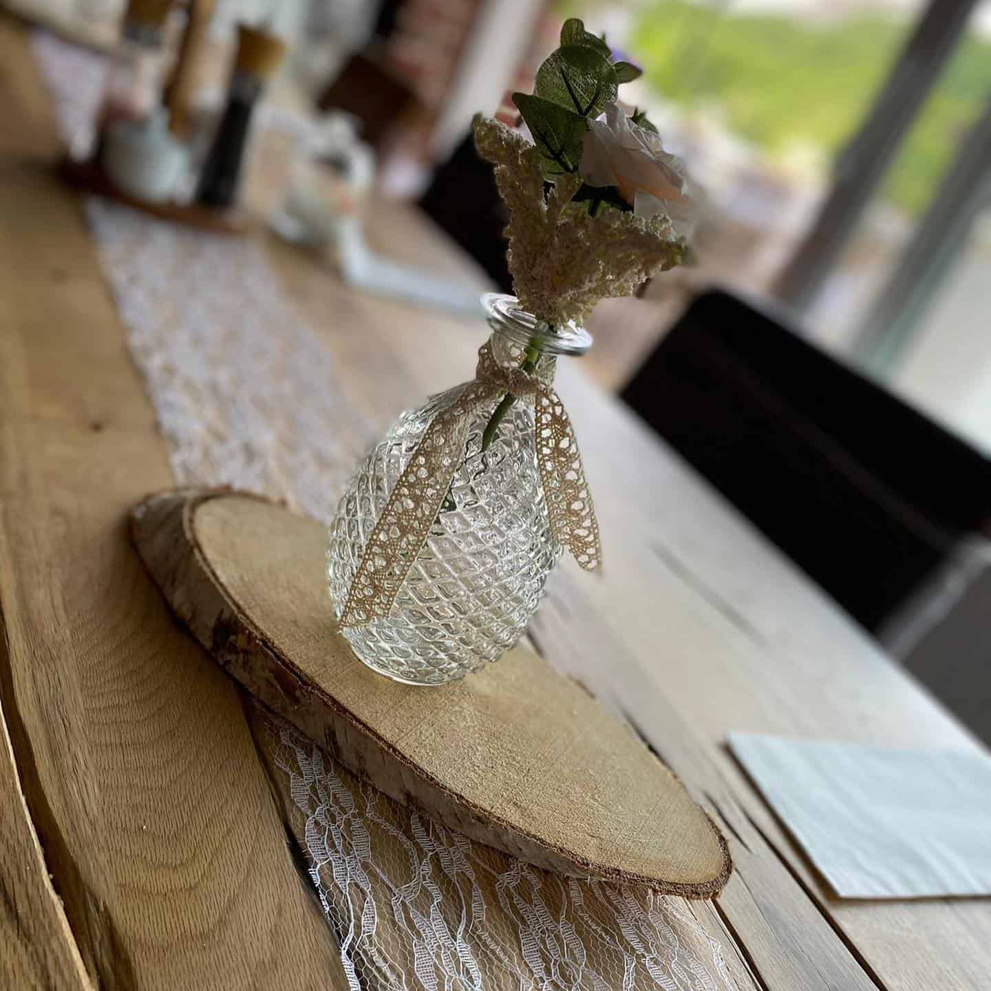 Elegante Vase mit Blumen, charmant auf Holzplatte für Hochzeits- oder Event-Dekoration. Filament, Vase mit Blumen auf Holzplatte, shabby chic, Hochzeit, Dekoration.