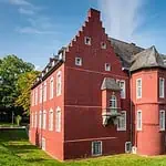 Alte rote Burg in Aachen, Germany, mit mittelalterlicher Architektur und grüner Umgebung.
