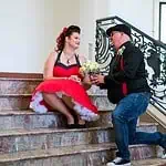 Verlobungsshooting mit Braut in rotem Kleid und Fotograf auf Treppe in beeindruckendem Haus.