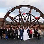 Fröhliche Hochzeitsgesellschaft vor einem historischen Rad in Aachen, feierlich und voller Freude.