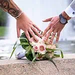 Blumenstrauß und Hände eines Paares, Hochzeitsfotografie in Aachen, verliebtes Paar mit Ringen und eleganten Outfits, romantische Kulisse.