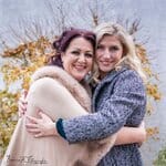 Zwei lachende Frauen umarmen sich am seeufer im Herbst, beste Freunde oder Schwestern, Natur- und Porträtfotografie, emotionale Momente festhalten.