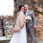 Elegantes Brautpaar im Winterhochzeits-Outfit vor alten Steinmauern, romantische Hochzeitsfotografie.