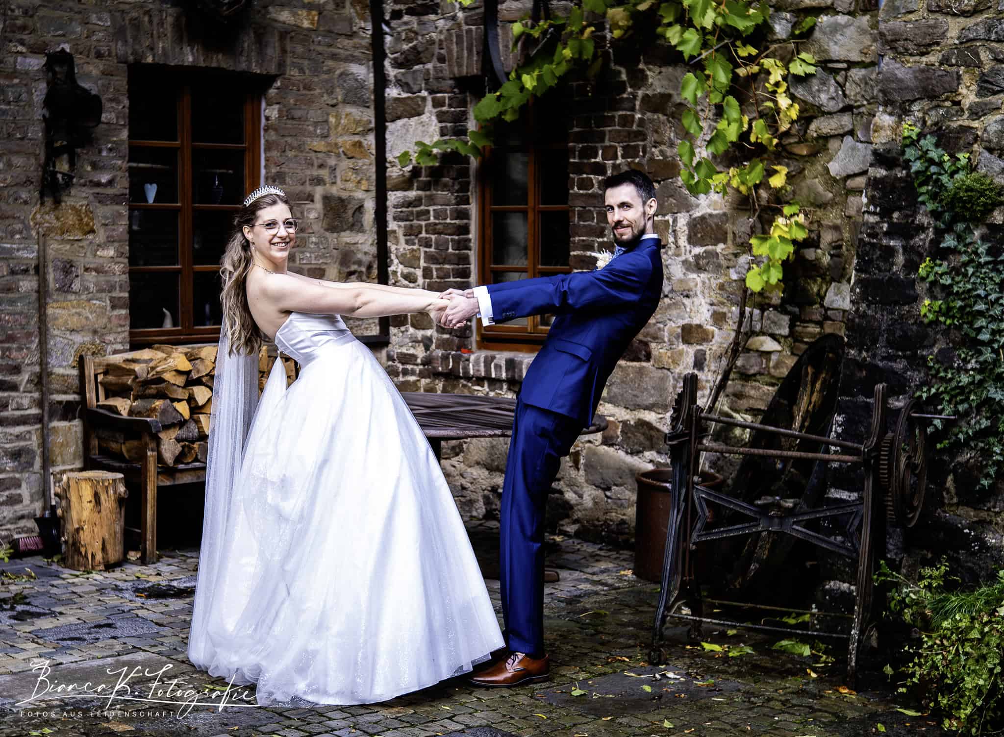 Hochzeitspaar tanzt vor rustikaler Steinmauer im Außenbereich.