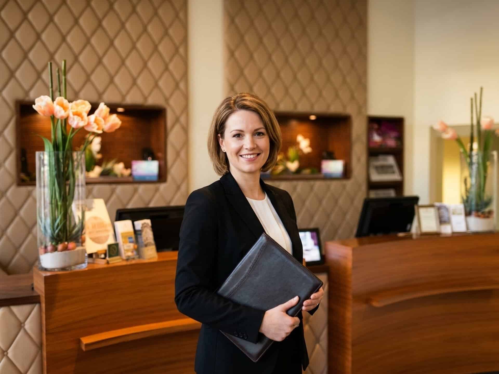 Mitarbeiterin in schwarzem Blazer und weißer Bluse steht mit einer Dokumentenmappe in der Lobby des Central-Hotel Kaiserhof.