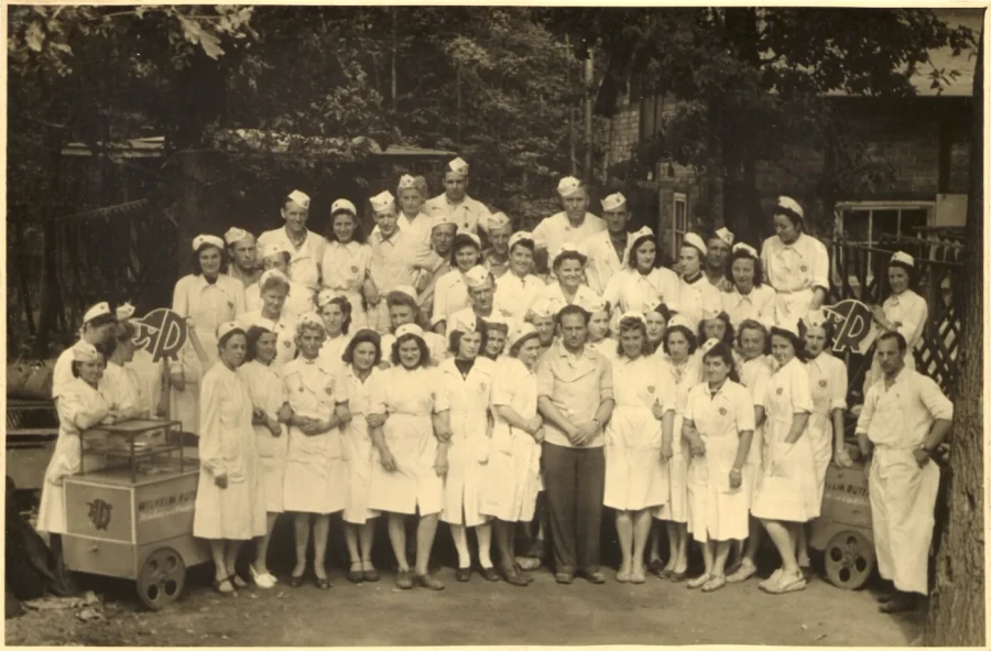 Gruppenfoto von knapp 50 Rüter-Mitarbeiterinnen und -Mitarbeitern in weißen Kitteln, flankiert von zwei mobilen Würstchen-Wagen