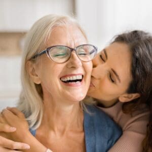 Tochter umarmt lachende Mutter und küsst sie