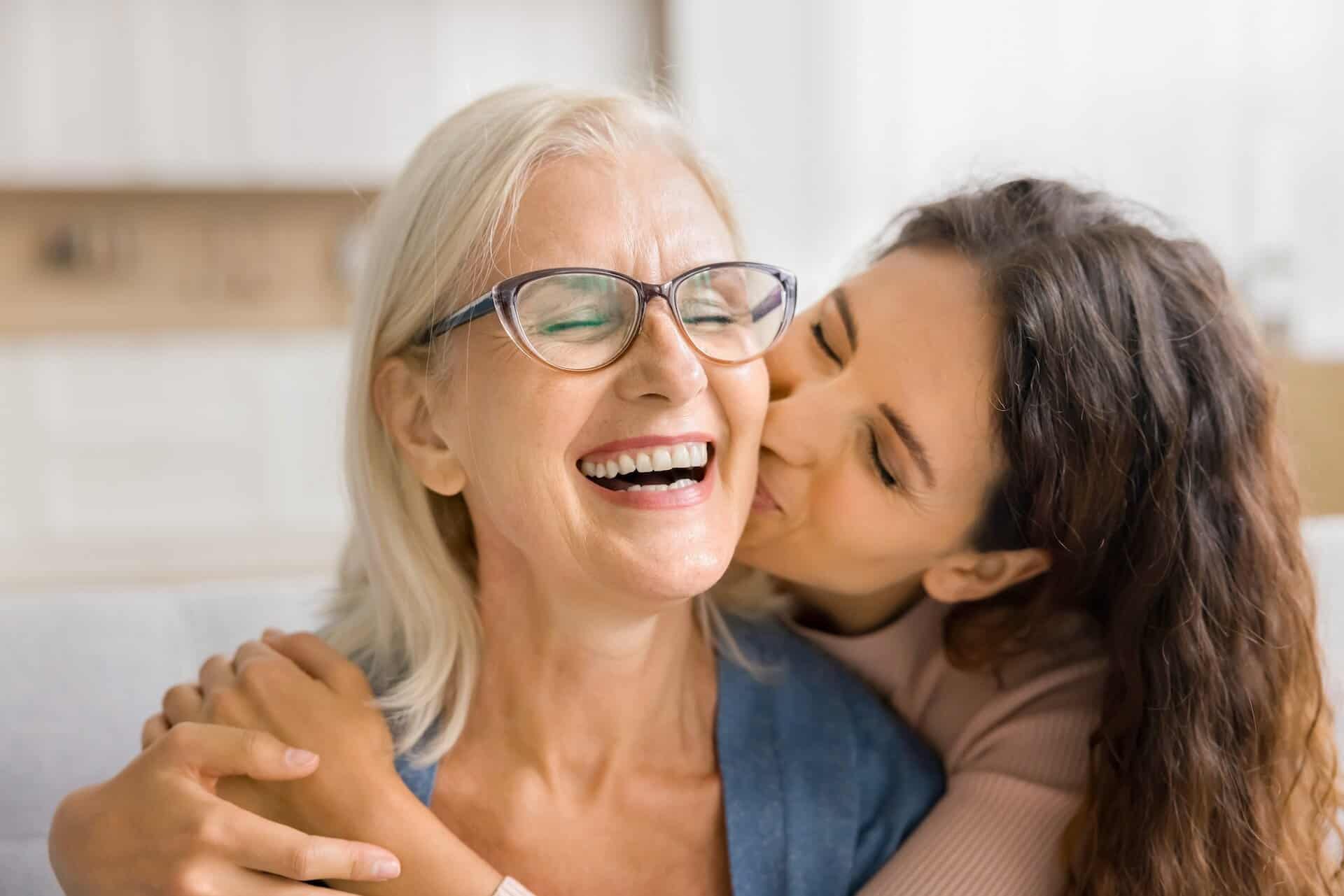 Tochter umarmt lachende Mutter und küsst sie