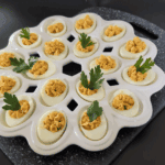 serving the creamy deviled eggs in white egg tray on gray speckled cutting board