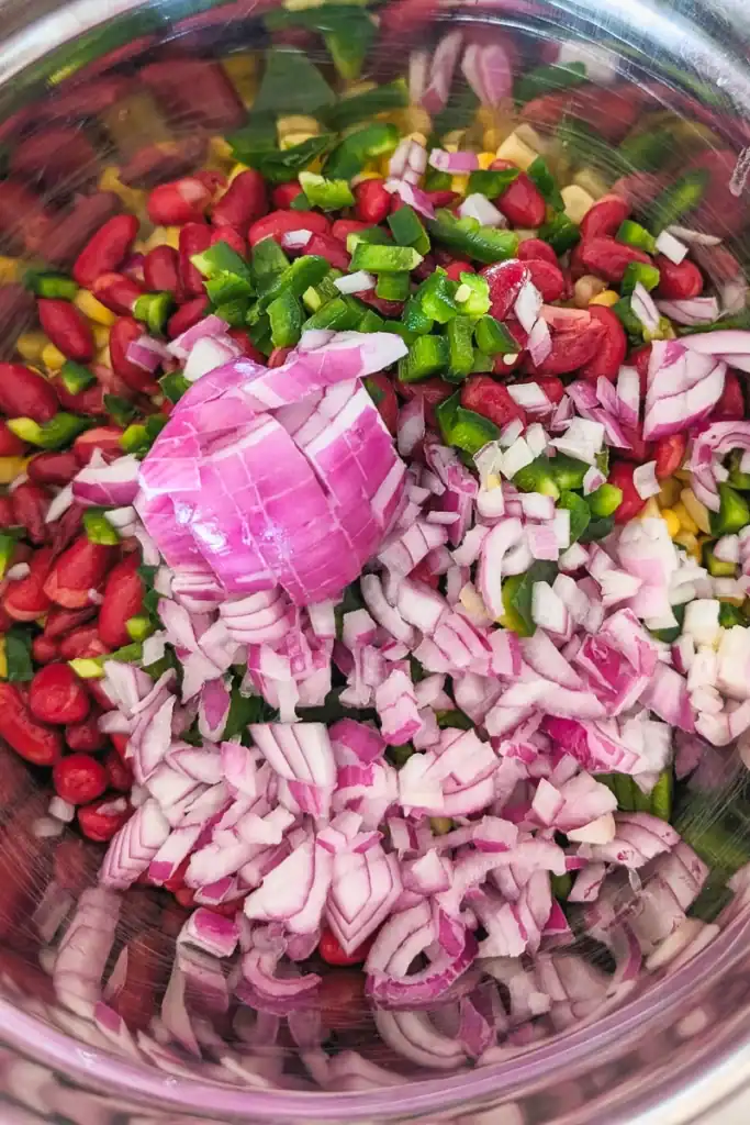 adding diced red onion to corn salad