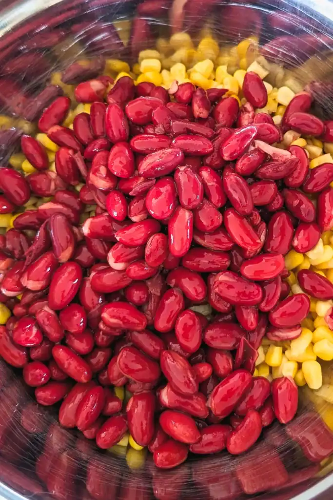adding drained kidney beans to corn in salad bowl