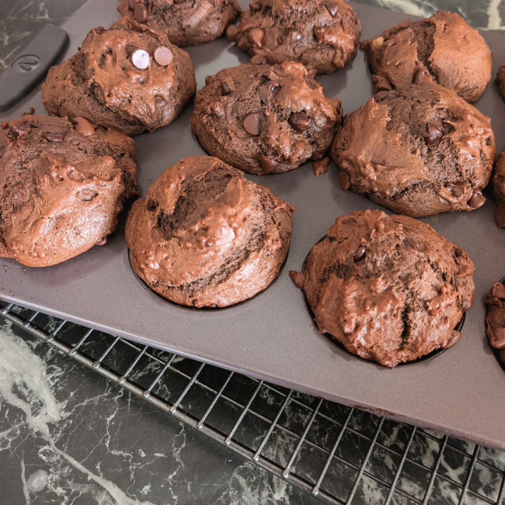 Freshly baked chocolate orange muffins with zest on a baking tray.