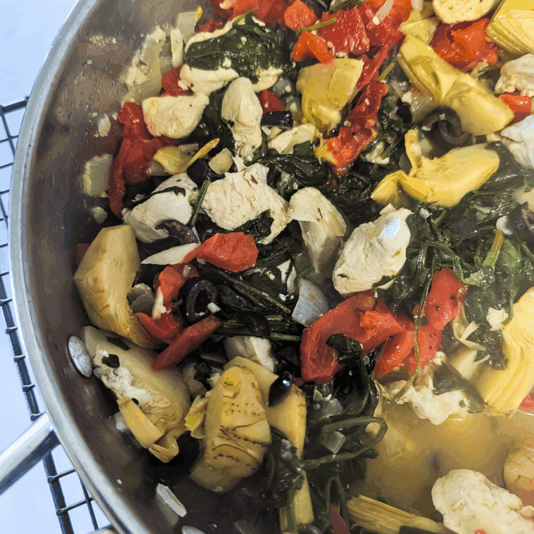 Freshly cooked vegetable stir-fry with spinach, artichokes, tomatoes, black olives, and chicken.