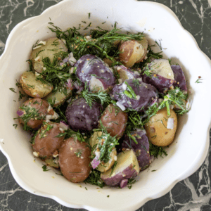 Colorful baby potatoes with dill and herbs in a white bowl.
