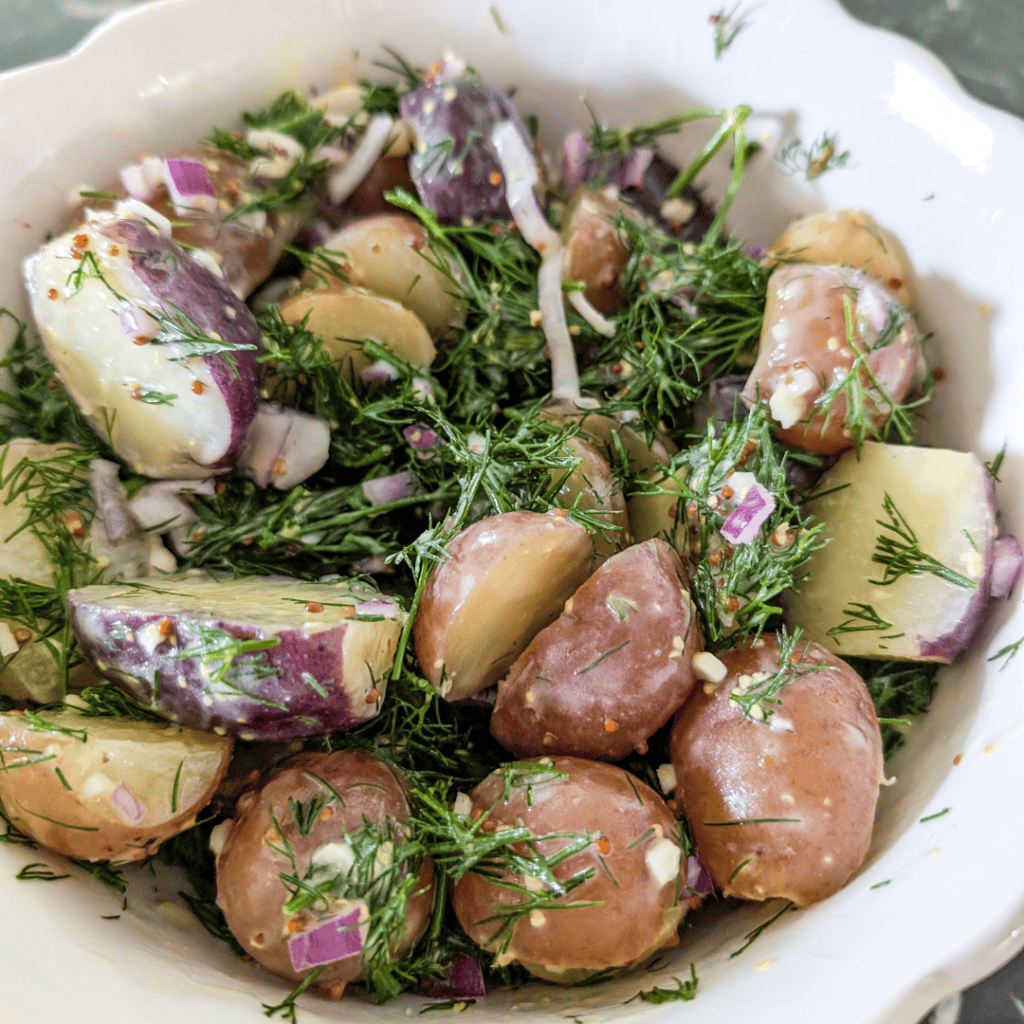 Baby potatoes with dill and red onion in a white bowl for salad.