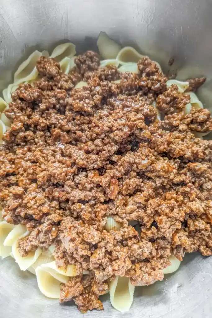 adding the taco meat to hot pasta in bowl