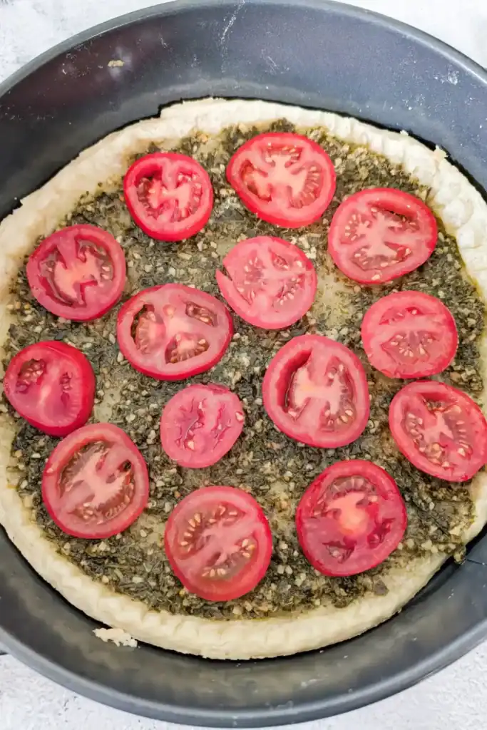 sliced cocktail tomatoes arranged on the surface of the basil layer of tart
