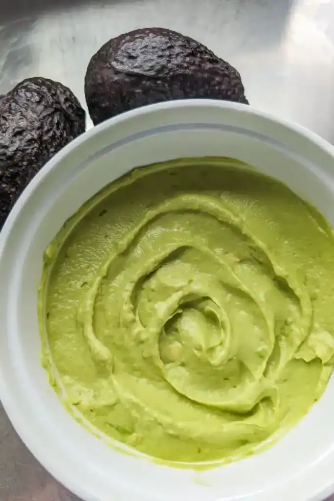 avocado crema finished in white bowl two whole avocados beside the bowl
