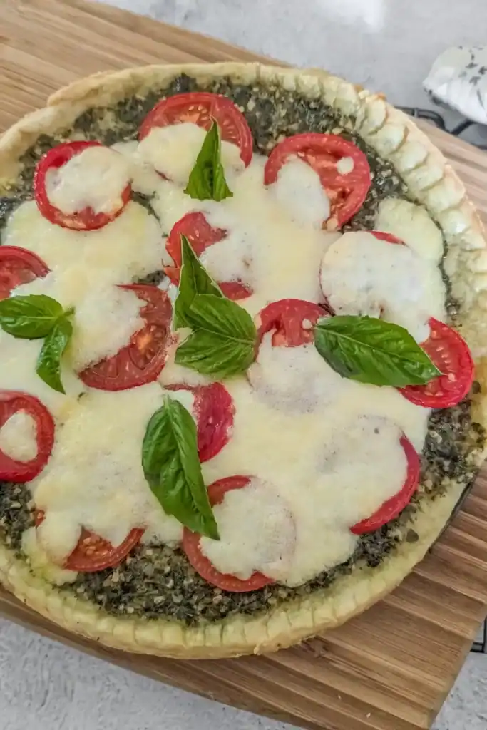 the baked tomato basil pesto tart with melted burrata cheese and fresh basil leaves on a wooden cutting board