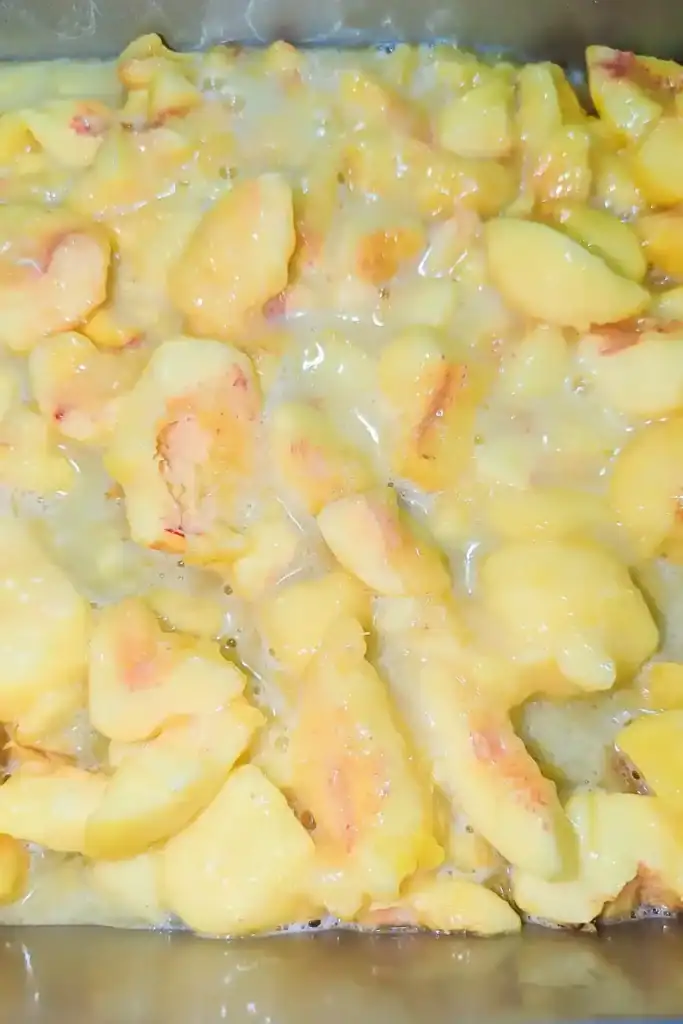 adding peach slices to the egg mixture in 8 by 8 baking dish