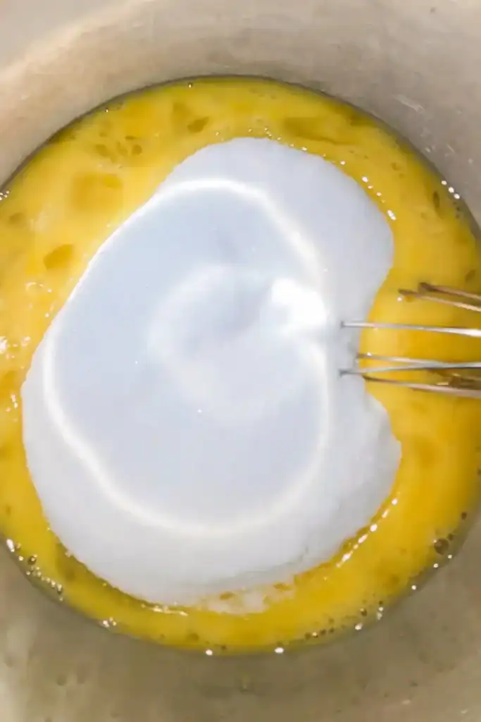 adding eggs and sugar in a mixing bowl