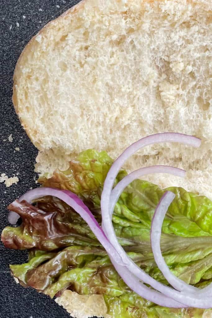 adding lettuce and onion to sandwich