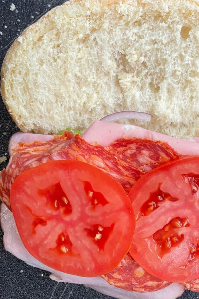 adding tomato to Italian scotch baps sandwich