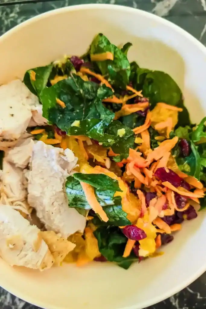 the finished kale salad with grilled chicken and fruit in a white bowl on a black marble table