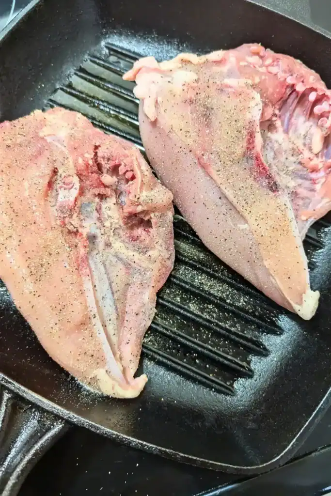 raw skinless chicken breasts skin side up in grill pan with salt and pepper on them