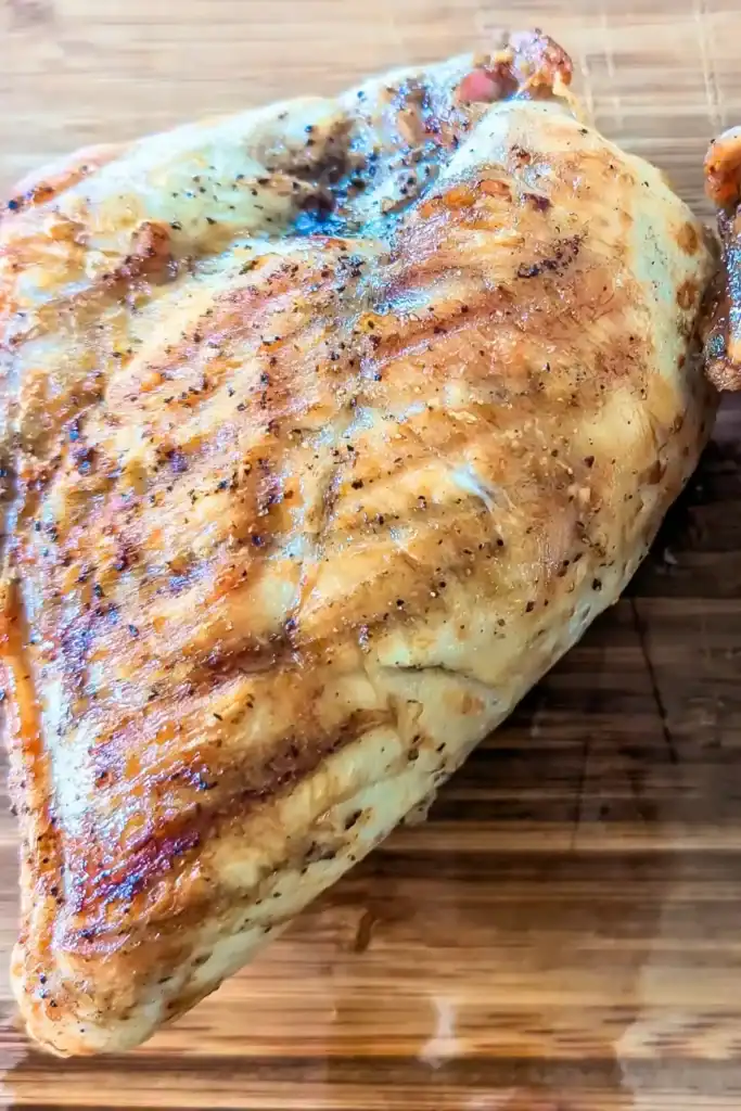 a grilled skinless chicken breast resting on wood cutting board