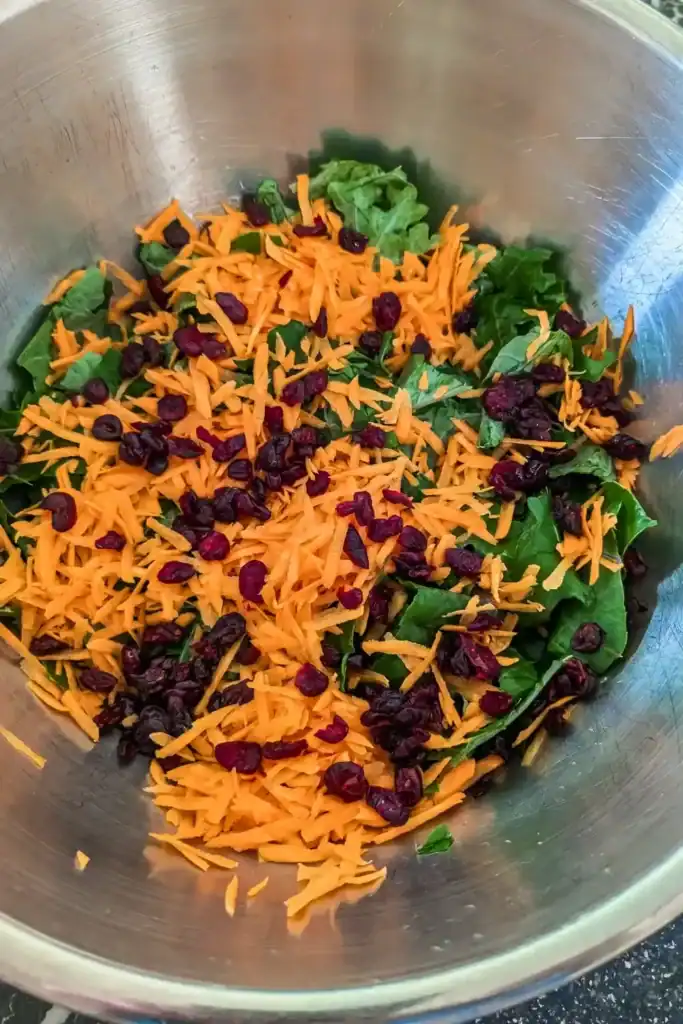 adding craisins dried cranberries to carrots and kale in salad bowl