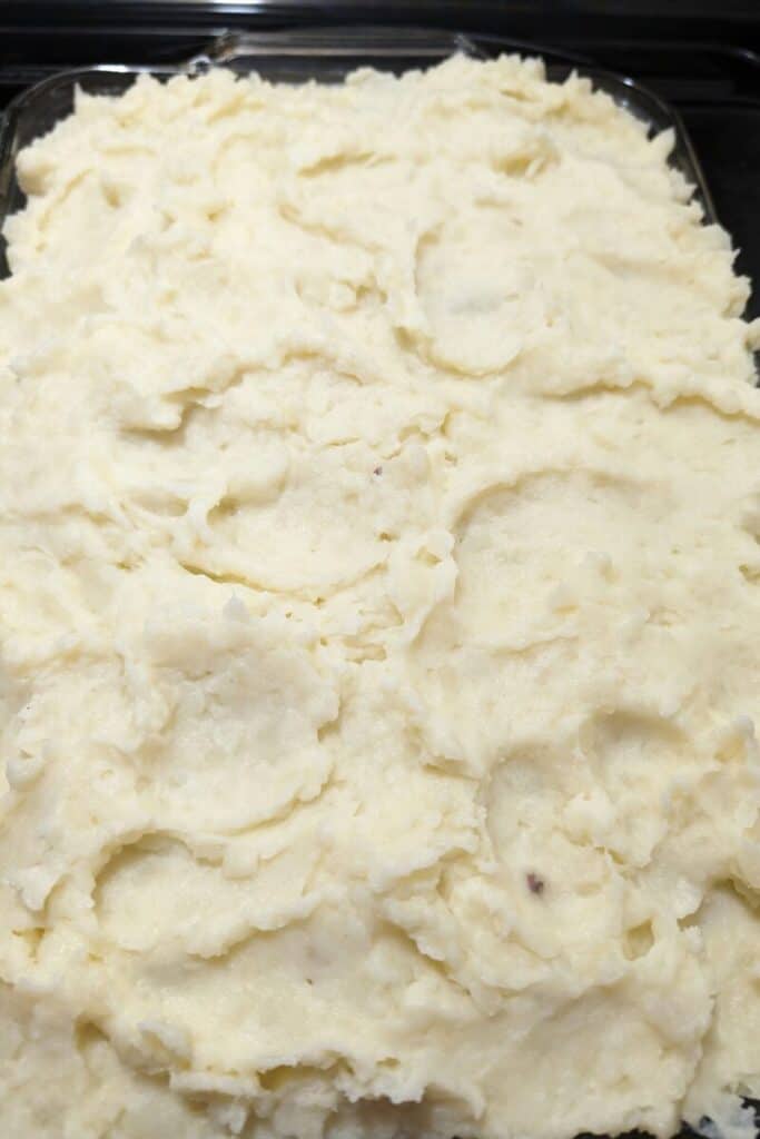 adding creamy mashed potatoes to shepherds pie