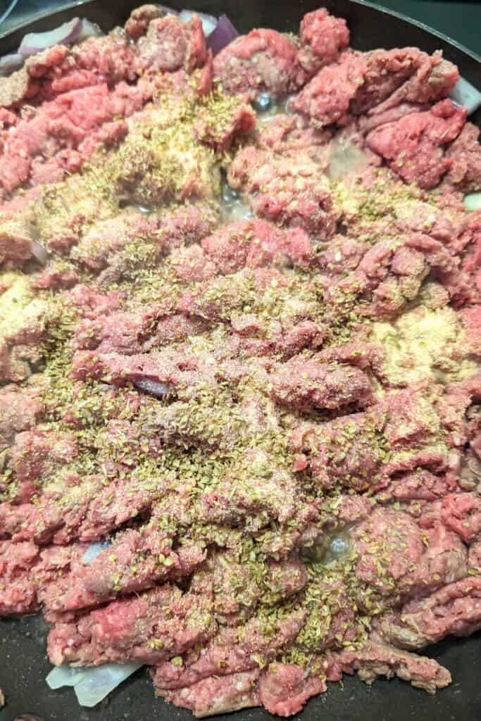 adding herbs and spices to meat mixture in frying pan