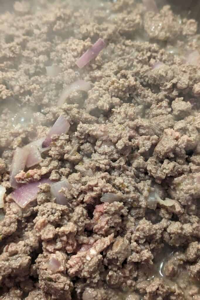 browning ground beef in frying pan with red onion