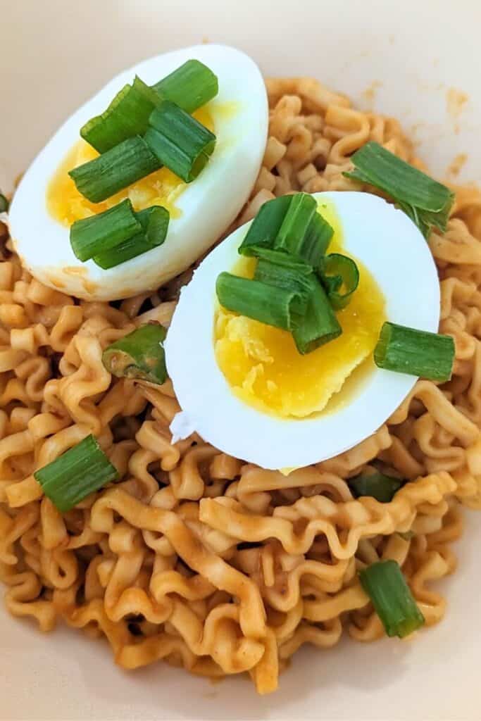 peeled jammy egg sits on top of peanut noodles with green onion garnish