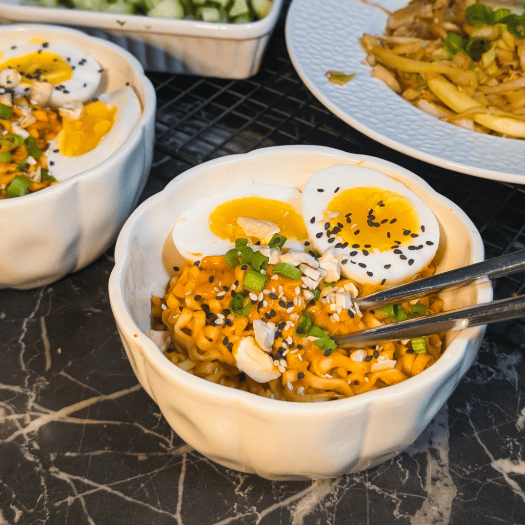 Close-up of spicy peanut noodles topped with jammy eggs and green onions.