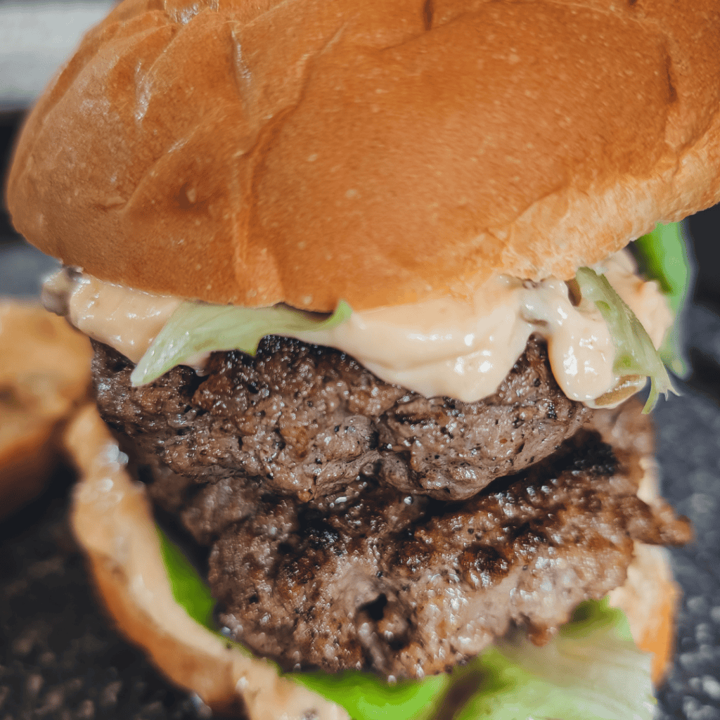 Delicious Con Queso Double Burger served in a skillet with melted cheese and fresh toppings. Perfect.